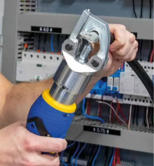 Elektrotechniker benutzt Crimpmaschine für dickes Kabel in Schaltschrank. Werkzeuge, Elektrosystem, Verkabelung.