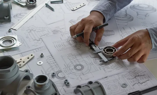 Ingenieur vermisst mit einer Schieblehre ein Metallteil auf technischen Zeichnungen, umgeben von Schrauben und Bauteilen.
