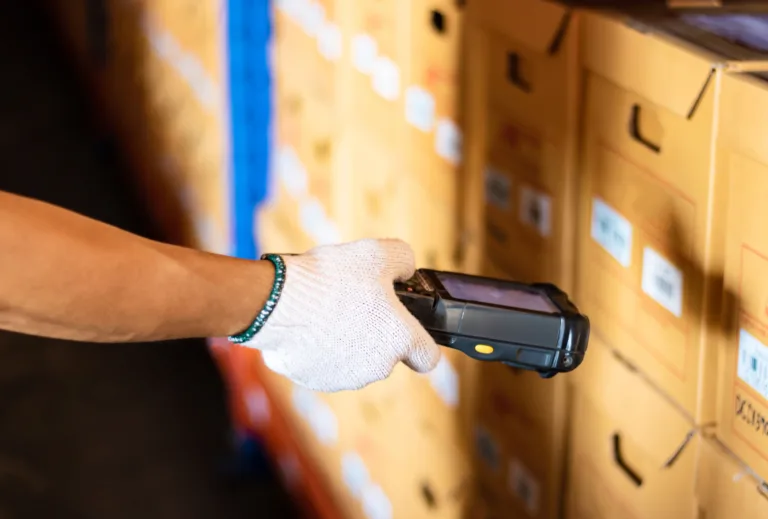 Person mit weißem Handschuh scannt mit Handscanner Barcodes auf Kartons im Lager, Logistik und Inventur effektiv unterstützend.
