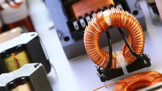 Kupferspule in Nahaufnahme, umgeben von elektronischen Bauteilen, zeigt Induktivität in der Elektrotechnik.