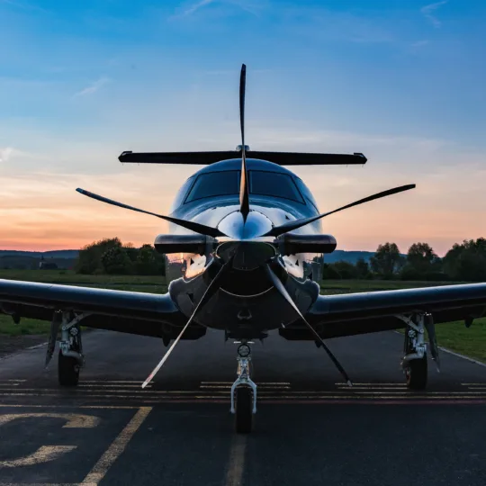 Propellerflugzeug auf Landebahn bei Sonnenuntergang, frontale Ansicht, blau-oranger Himmel, Flugzeug, Dämmerung.