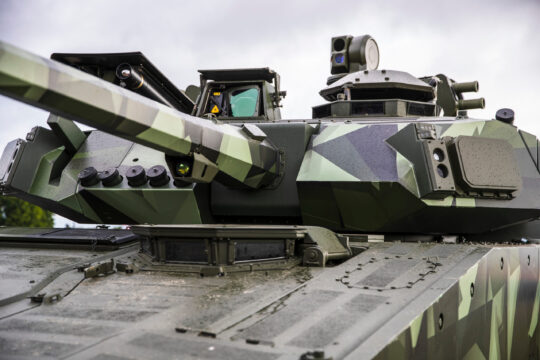 Kampffahrzeug mit Tarnmuster und Bewaffnung, Nahaufnahme eines gepanzerten Turms bei bewölktem Himmel.